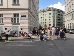 A group of people gathering on a street corner in summer, painting, chatting and having fun